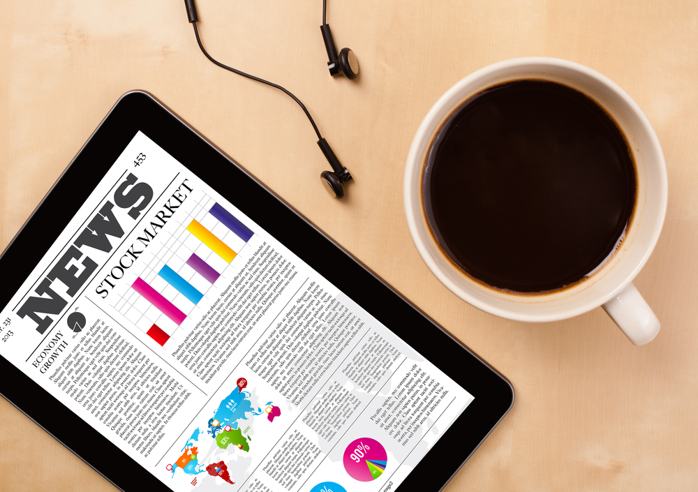 Workplace with tablet pc showing latest news and a cup of coffee on a wooden work table close-up